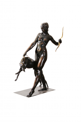 Statue of woman holding a bow in her left hand and restraining a leaping dog with the right hand. 