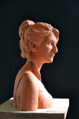 Terra cotta bust of woman with hair in pony tail against black background